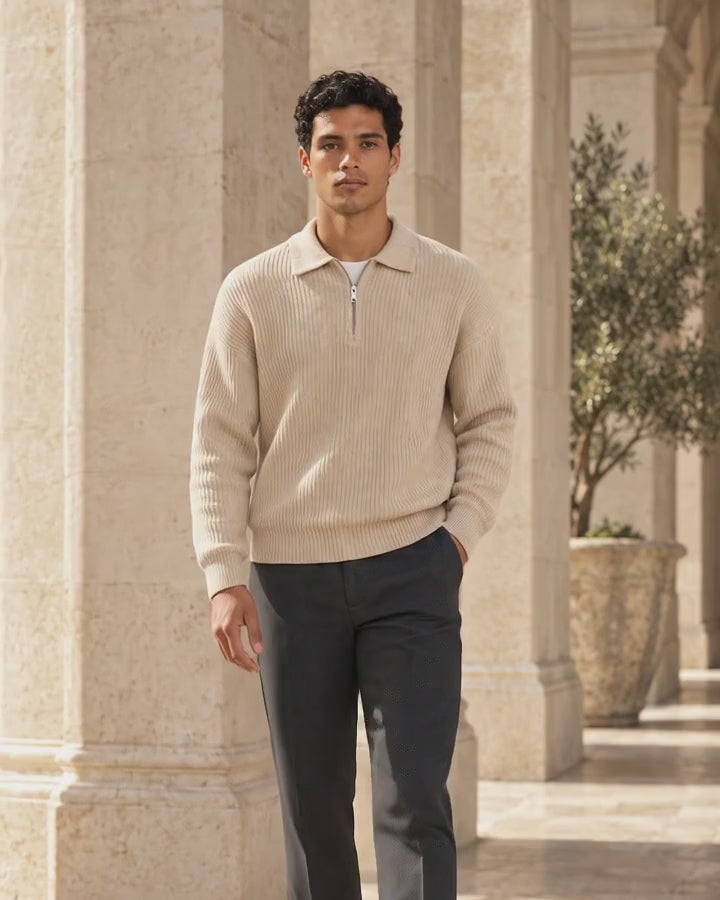Vídeo editorial VALERUME: hombre con jersey beige de media cremallera y mujer con blusa azul de hombros descubiertos, en arquitectura cálida de piedra.
