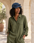 Mujer VALERUME con gorra de denim azul marino lavado, visera curva y lazo frontal, de cuerpo entero en un patio de piedra cálida.