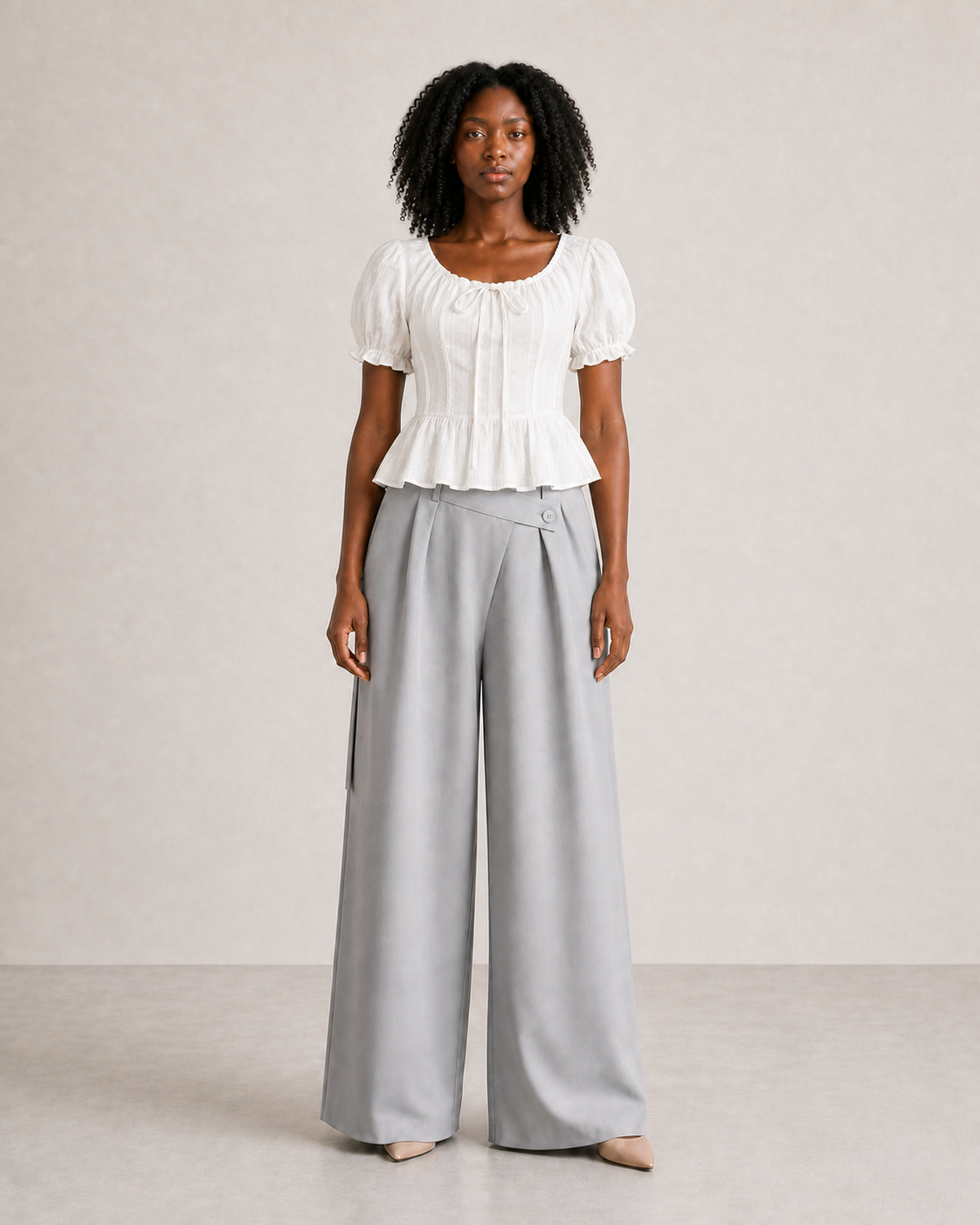 Mujer con top peplum blanco de mangas abullonadas y pantalón gris, vista frontal de cuerpo entero
